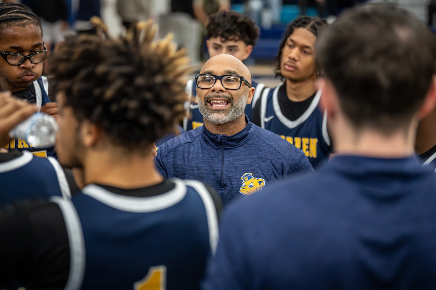 A coach speaking with his young players in a huddle inside the gym
