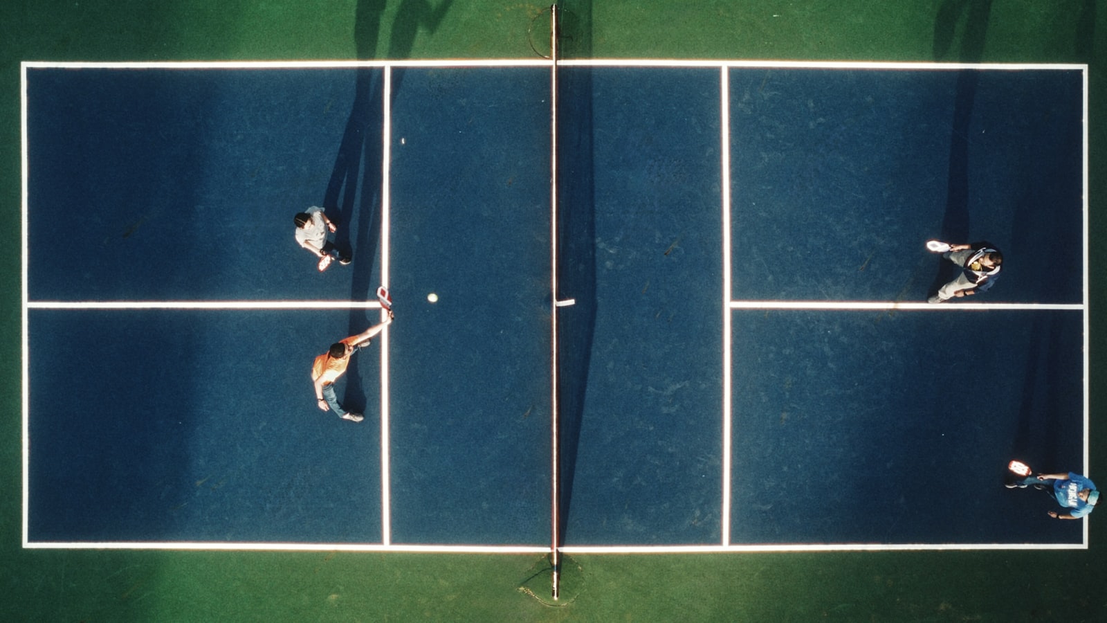 An overhead view of four players mid-game on a blue pickleball court