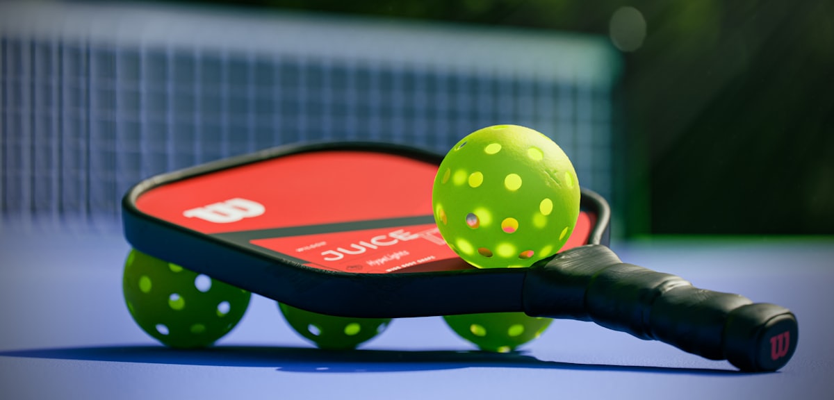 A pickleball paddle and bright yellow balls on a blue court